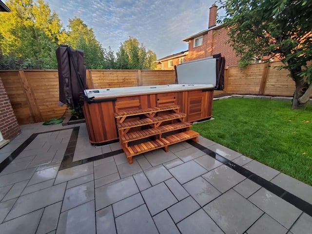 Guelph backyard interlocking patio with hot tub surround, dark stone border accent and cedar privacy fence installed by BCI Landscaping