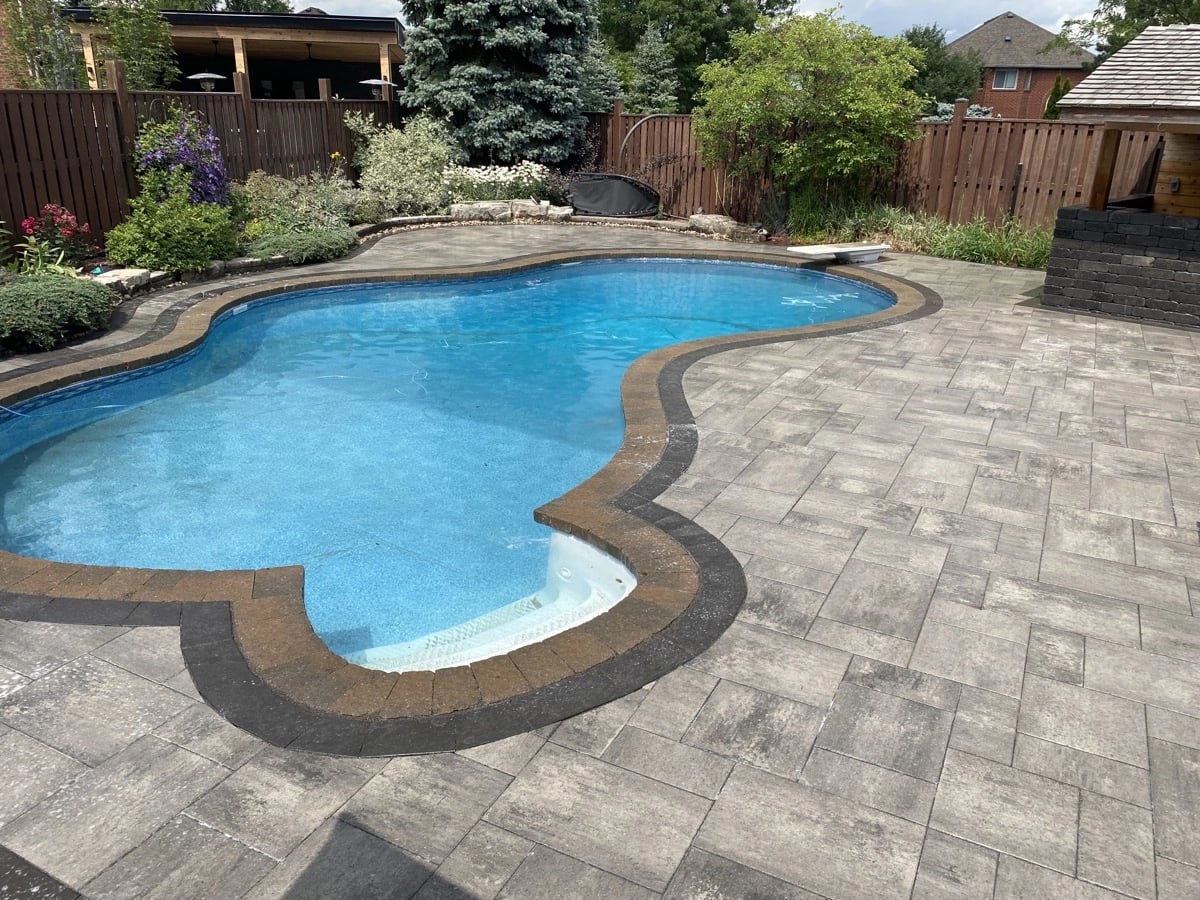 Freeform pool with large-format interlock paver deck and charcoal coping, pool landscaping Guelph by BCI Landscaping