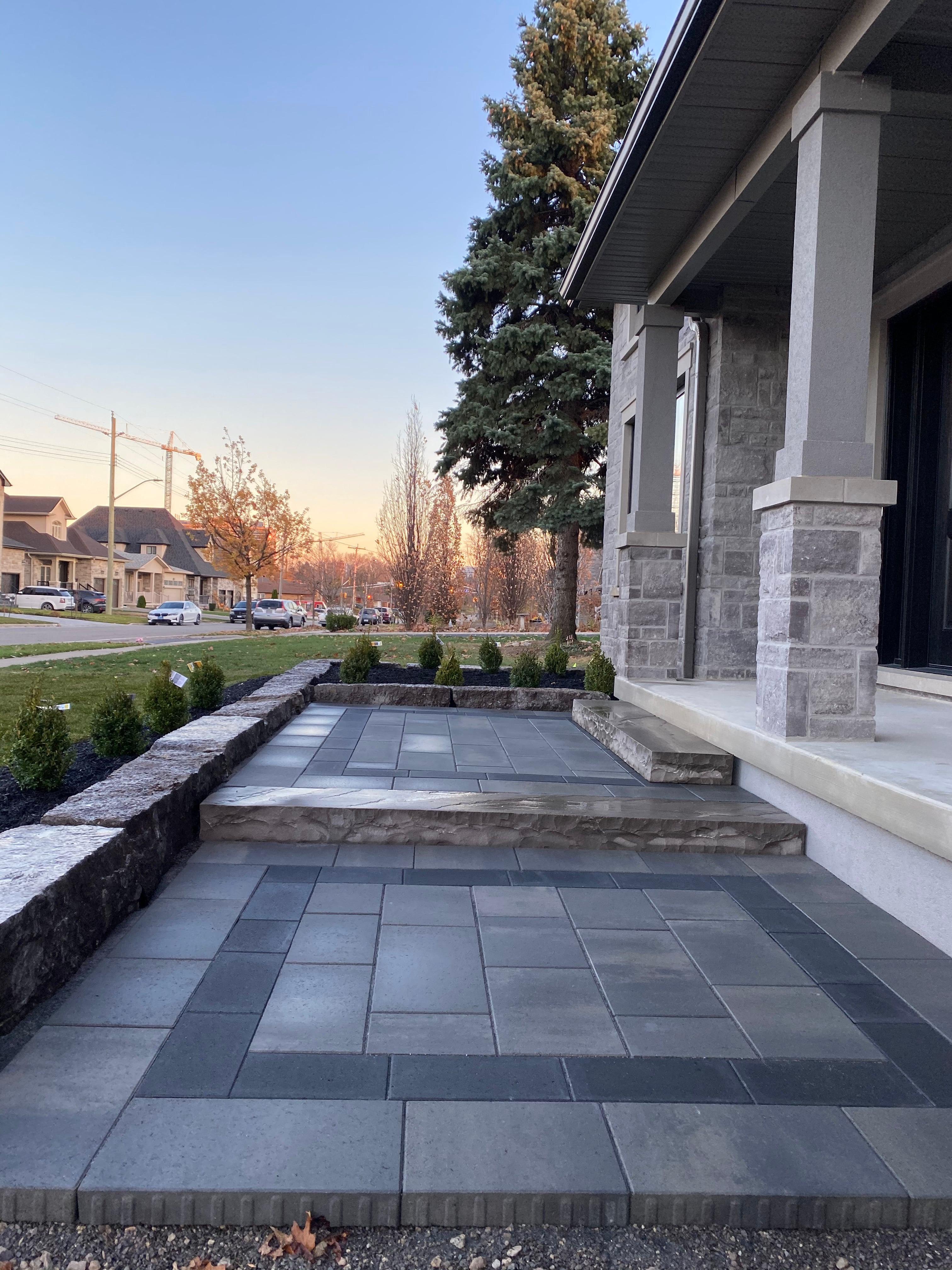 Guelph front entrance interlocking patio with stone steps and garden beds at sunset by BCI Landscaping