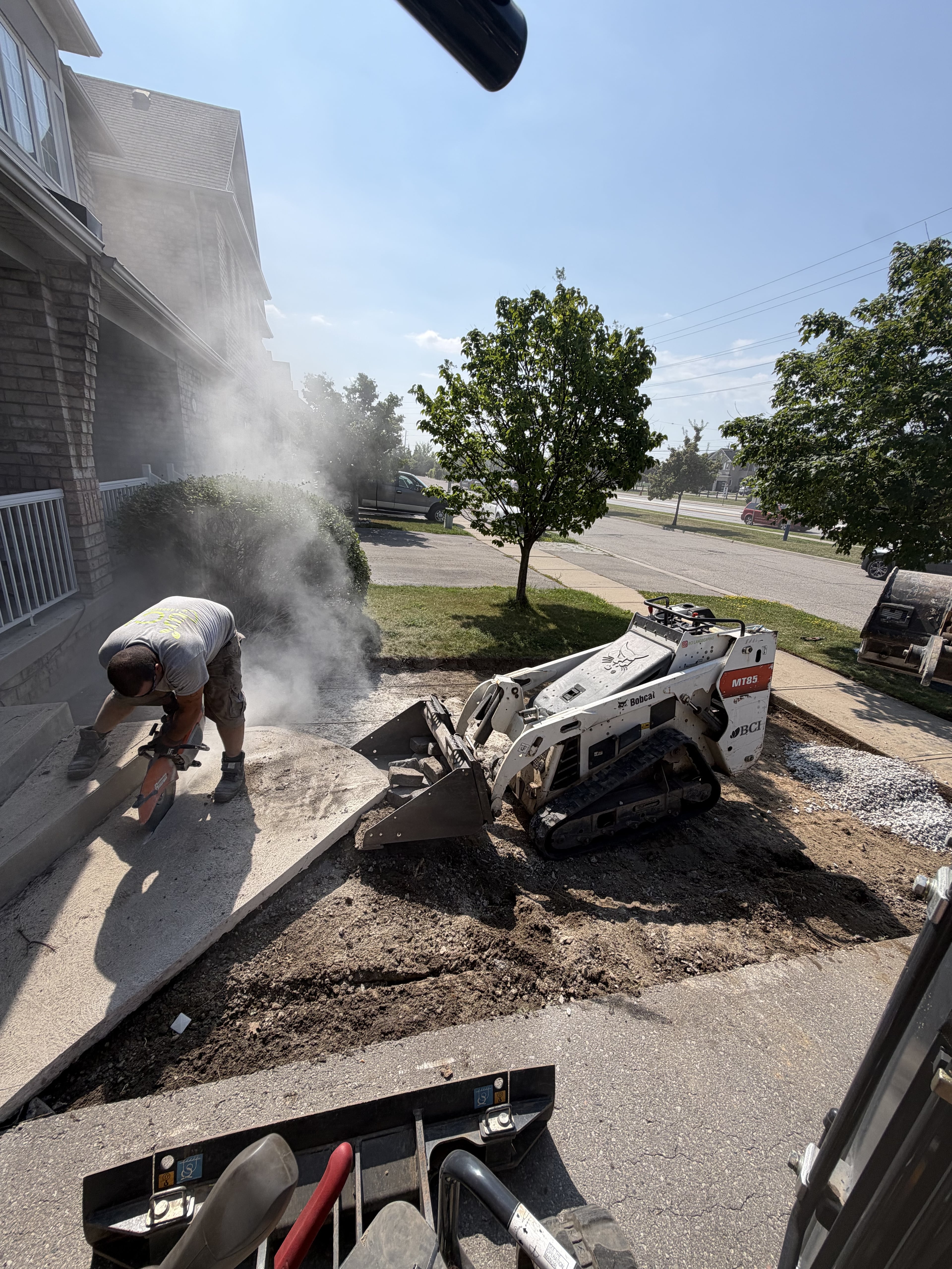 BCI Landscaping crew member cutting stone on a Guelph landscaping job site with mini-excavator in background