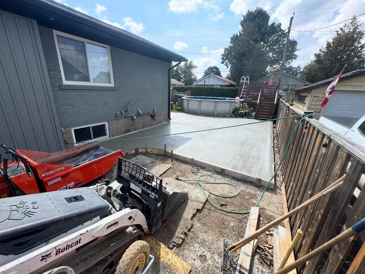 Fresh concrete pad poured beside a home with skid steer on site, concrete pads Guelph by BCI Landscaping