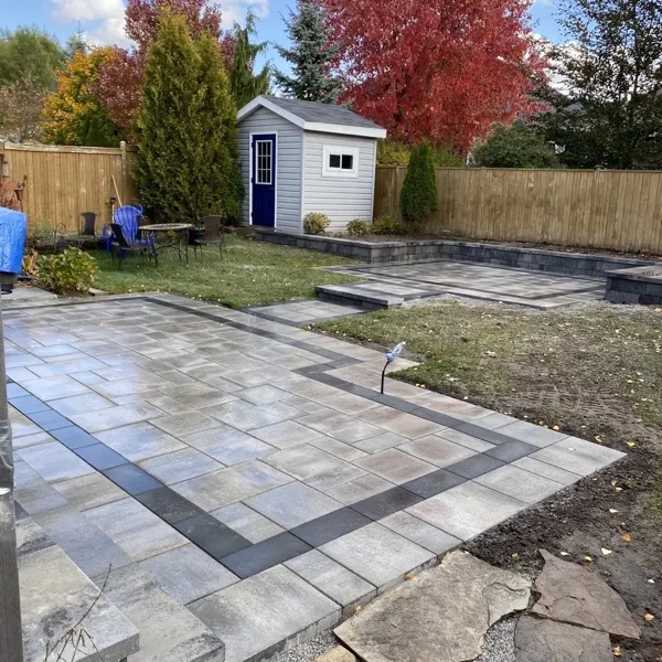 Multi-level interlocking patio with charcoal border and raised back platform in a Guelph backyard